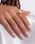 Hand model wearing Starlit Whisper press-on nails with translucent nude pink bases, white star patterns, silver star accents, silver beads, and gold rings on satin fabric