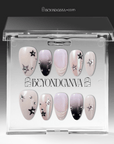 Packaging display of Stellar Muse press-on nails in a clear Beyondcanva case with black and silver star charms, rhinestones, silver beads, nude pink bases, and black gradient accents