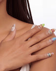 Sunset Gypsy handmade press-on nails shown in a close-up hand pose with nude bases, colorful gems, and gold accents