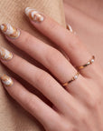 Close-up of a hand wearing brown and white shell-pattern press-on nails with gold rings on a beige background.
