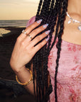 Beach lifestyle shot of Swan Ballet iridescent press-on nails worn with pearl jewelry and a pink dress