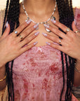 Model wearing Swan Ballet iridescent press-on nails with pearl jewelry and a pink floral dress