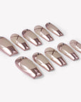 Angled flat lay of Swan Lake Dream press-on nails with rose gold metallic French tips, nude jelly bases, crisscross lines, and rhinestones