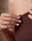 Hand model wearing Timeless Serenity press-on nails with nude bases, black French tips, and a white 3D flower while holding a brown ribbed top