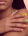 Hand model wearing Tropical Jelly Bloom press-on nails in yellow, green, pink, and orange floral designs