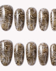 Flat lay of beige and brown snakeprint press-on nails with a glossy finish in assorted almond and coffin shapes