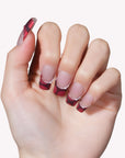 Close-up of a hand model wearing Vintage Ruby press-on nails in glossy red and black with pearl accents