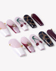 Angled flat lay of Wild Cherry press-on nails with burgundy cherry art, leopard print, sheer pink bases, and gold accents
