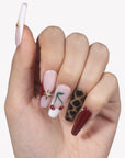 Hand model wearing Wild Cherry press-on nails with pink sheer bases, burgundy accents, cherry nail art, leopard print, and gold details