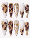 Wild Majesty press-on nails with tan leopard print, white bases, raised gold dot accents, gold charms, and metallic gold stiletto tips
