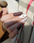 Hand model wearing Winter Serenade press-on nails with deep purple rhinestone tips, a white 3D flower, and nude plaid accent nails