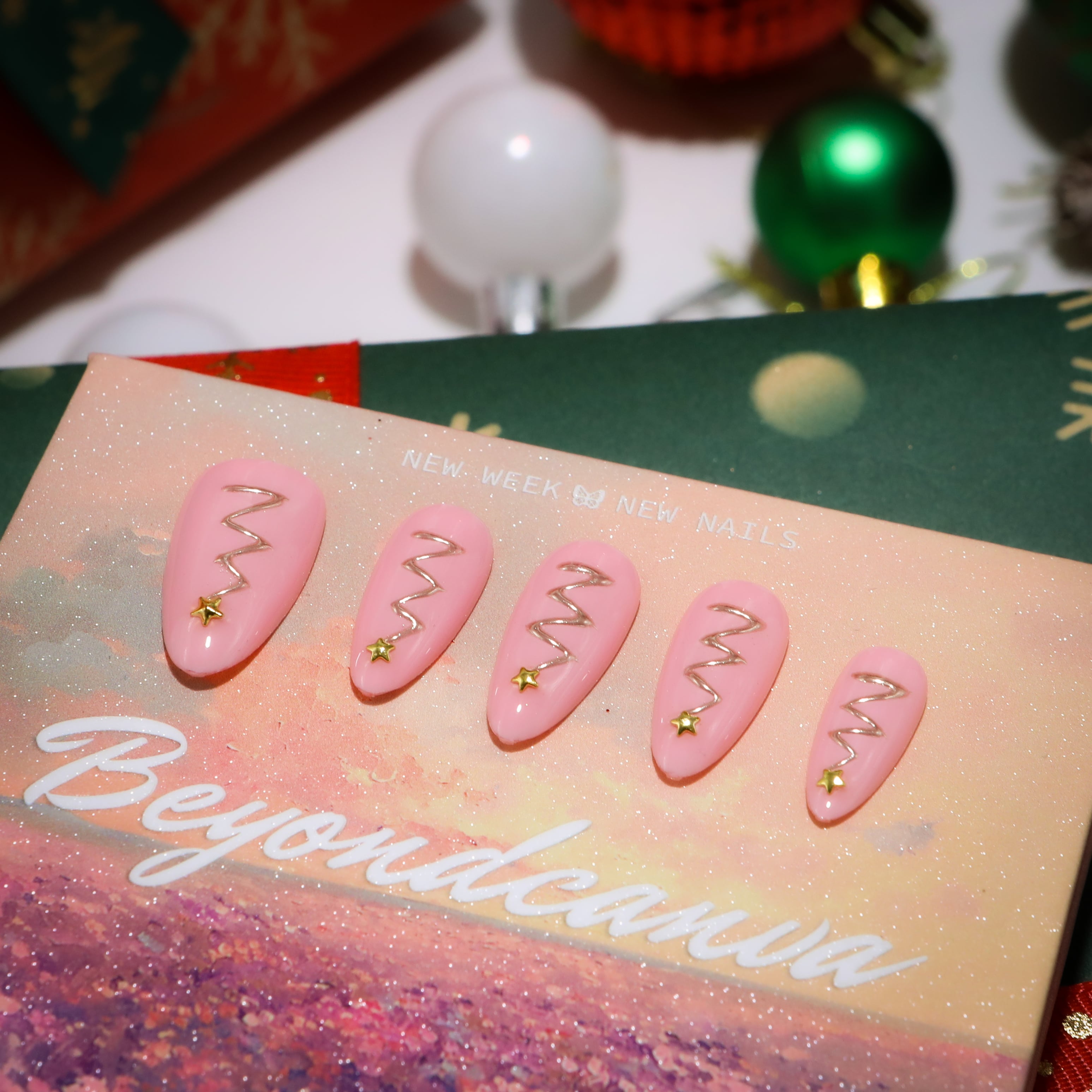 This beyondcanva press-on nail set features pastel pink nails with festive gold zigzag accents and star embellishments, resembling Christmas trees. Packaged in a luxurious pink box, it’s perfect for a chic holiday look.