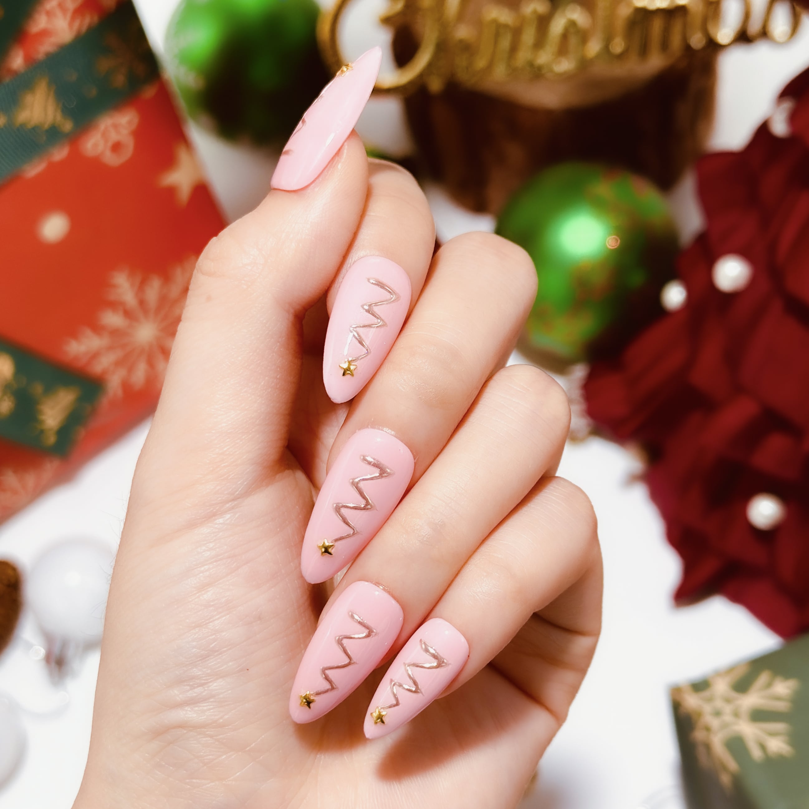 This beyondcanva press-on nail set features pastel pink nails with festive gold zigzag accents and star embellishments, resembling Christmas trees. Packaged in a luxurious pink box, it’s perfect for a chic holiday look.