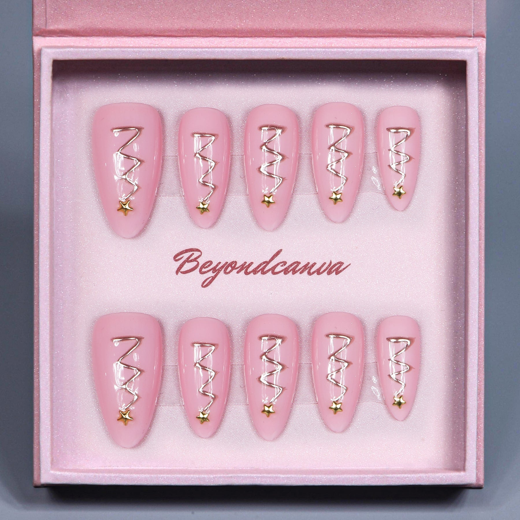 This beyondcanva press-on nail set features pastel pink nails with festive gold zigzag accents and star embellishments, resembling Christmas trees. Packaged in a luxurious pink box, it’s perfect for a chic holiday look.