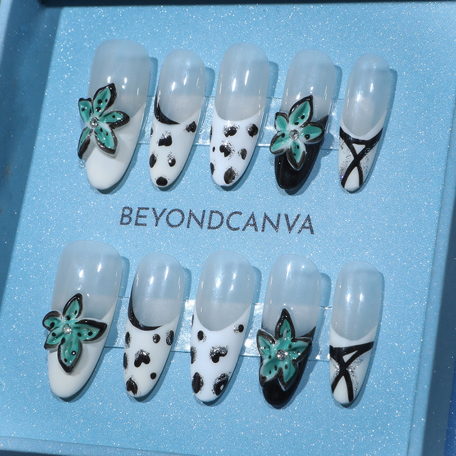 BEYONDCANVA press-on nails set with black and white patterns, teal floral accents, and crisscross designs, presented in a blue box and on a reflective surface.