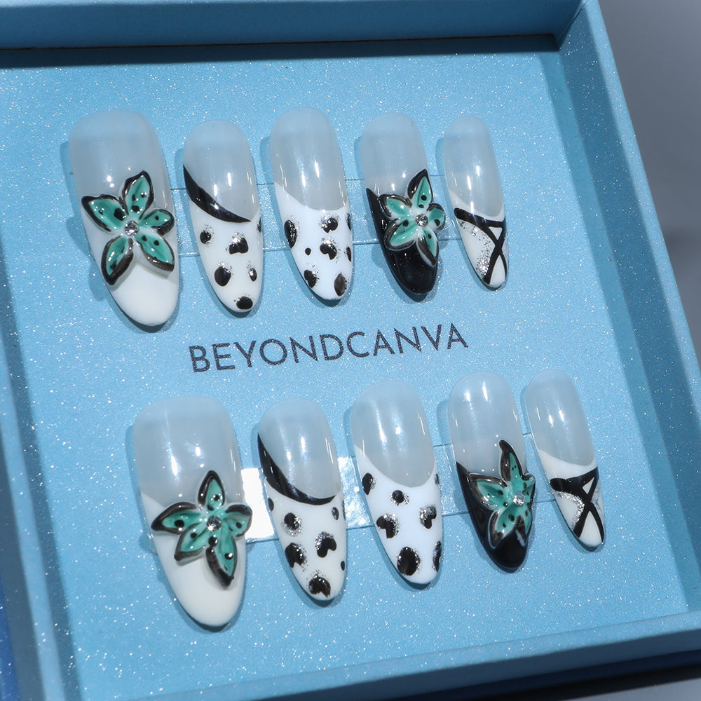 BEYONDCANVA press-on nails set with black and white patterns, teal floral accents, and crisscross designs, presented in a blue box and on a reflective surface.