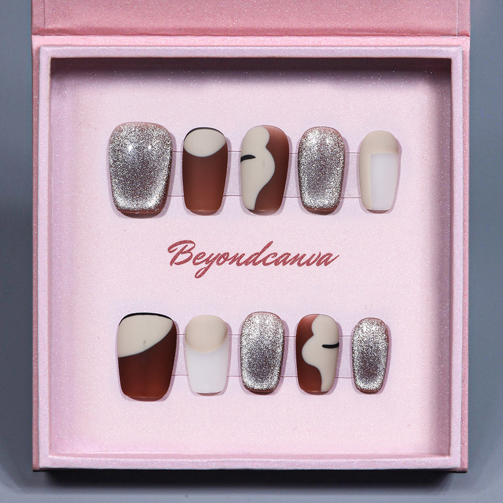 BEYONDCANVA press-on nails set showcasing individual nails with matte brown, cream, and glitter designs, captured on a reflective surface.