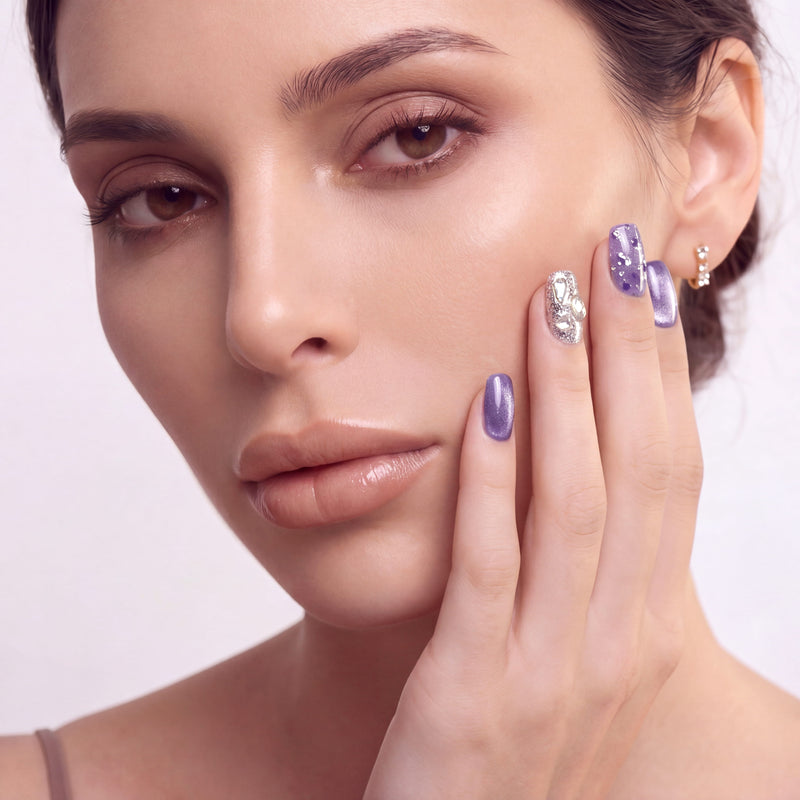 Hand model wearing Amethyst Veil press-on nails with shimmering purple polish, translucent tips, and silver gemstone accents