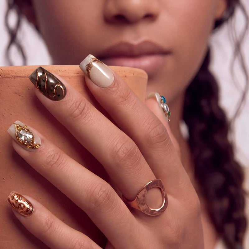 Model holding a terracotta block while wearing gold and ivory press-on nails in a close-up portrait.