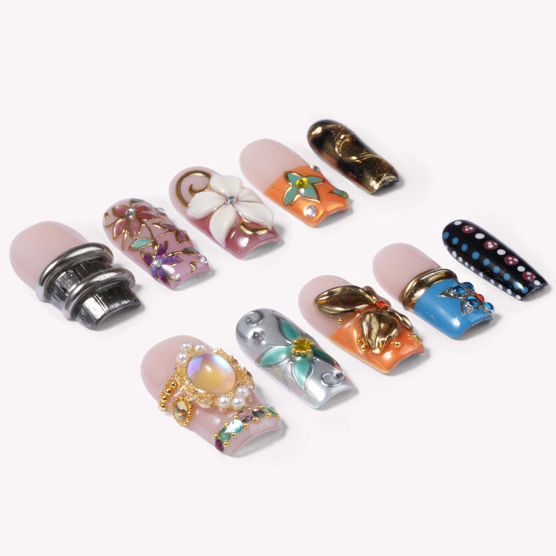 Angled flat lay of ornate press-on nails with 3D florals, pearls, butterfly charms, and multicolored rhinestones.
