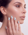 Hand model posing with silver-white press-on nails, blue rhinestones, and glitter tips against a white background.