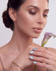 Hand model holding a lily stem while wearing silver-white press-on nails with blue rhinestones and glitter tips.