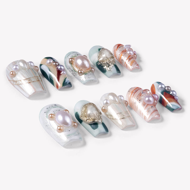 Angled flat lay of Aqua Relic press-on nails with pearls, gold shell charms, sea green accents, and orange marble patterns