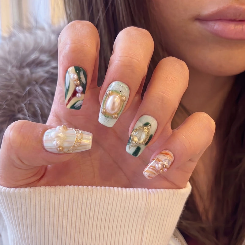 Hand model wearing Aqua Relic press-on nails with pearls, gold shell charms, sea green accents, and orange marble details
