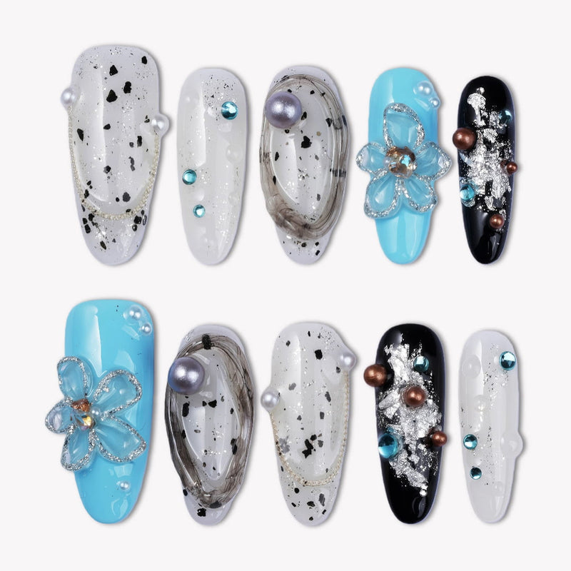 Flat lay of Artisian Orbit press-on nails with white, black, and blue accents, pearl details, and gem embellishments