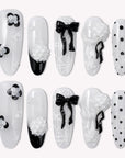 Flat lay of Atelier Hydrangeas press-on nail swatches with black and white floral accents, bows, and polka dots