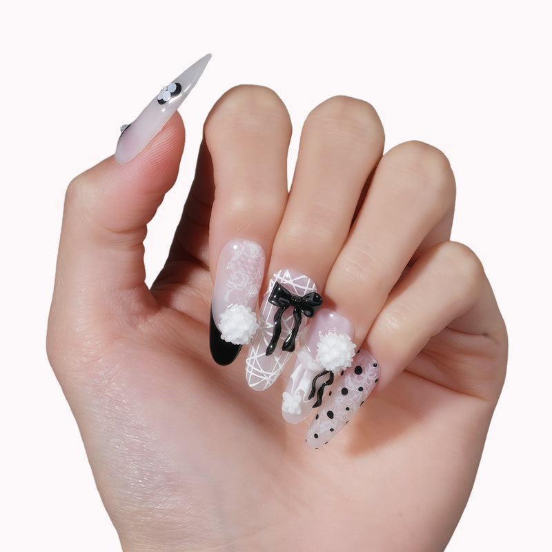 Hand model wearing Atelier Hydrangeas press-on nails with black and white floral accents, bows, and polka dots