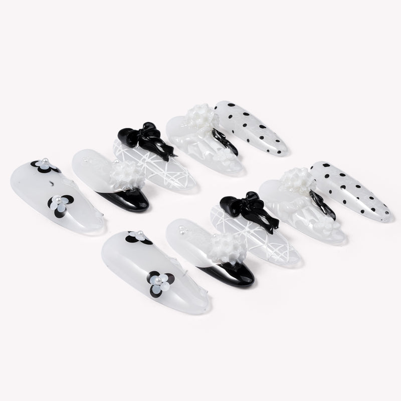 Flat lay of Atelier Hydrangeas press-on nails with black and white floral accents, bows, and polka dots arranged in two rows