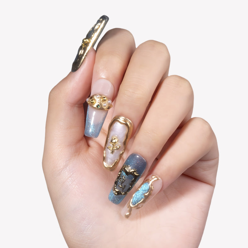 Hand model wearing Aurelia blue, pearl and gold sculpted press-on nails with metallic relief details on white