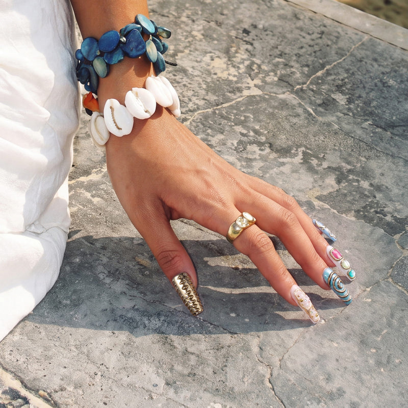 Sunlit hand wearing Aurelia turquoise, pearl and gold statement press-on nails beside layered shell bracelets