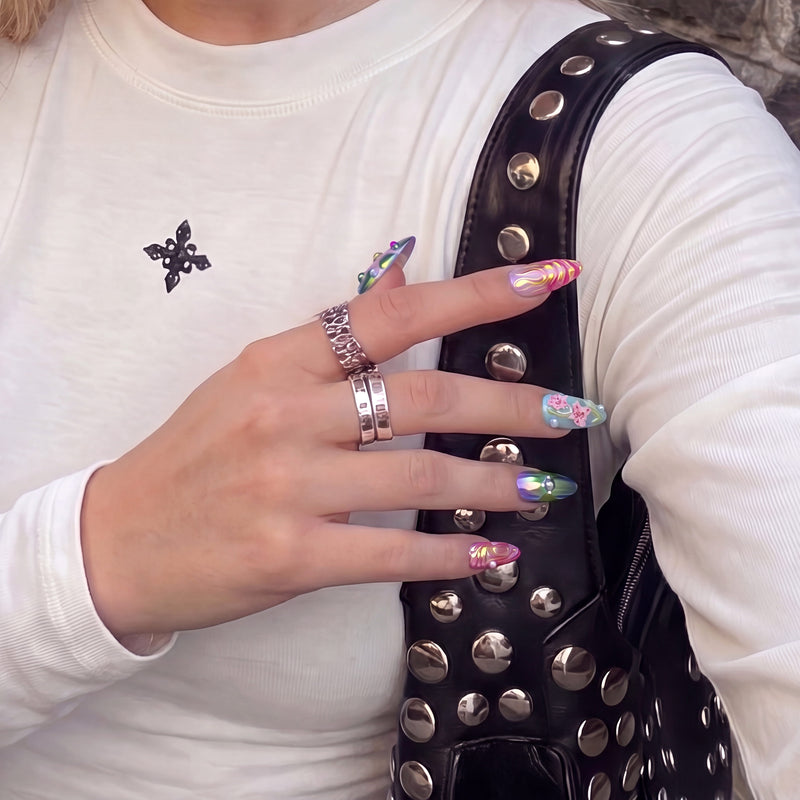 Hand model wearing Aurora Petals colorful iridescent press-on nails beside a black studded bag and white top