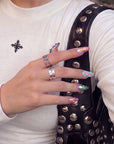 Hand model wearing Aurora Petals colorful iridescent press-on nails beside a black studded bag and white top