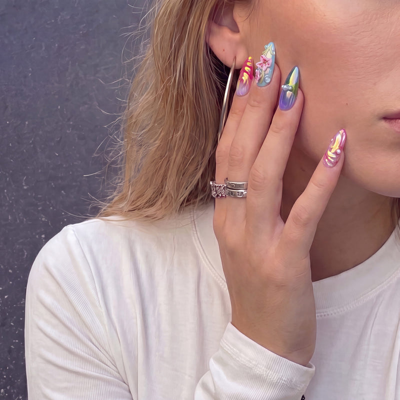 Face close-up of a model wearing Aurora Petals iridescent press-on nails with raised pink flowers, pearls and colorful swirls