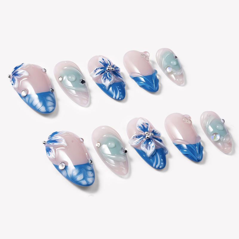 Angled flat lay of Azure Bloom press-on nails with pink bases, blue floral tips, aqua swirls, and silver gems
