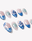 Angled flat lay of Azure Bloom press-on nails with pink bases, blue floral tips, aqua swirls, and silver gems