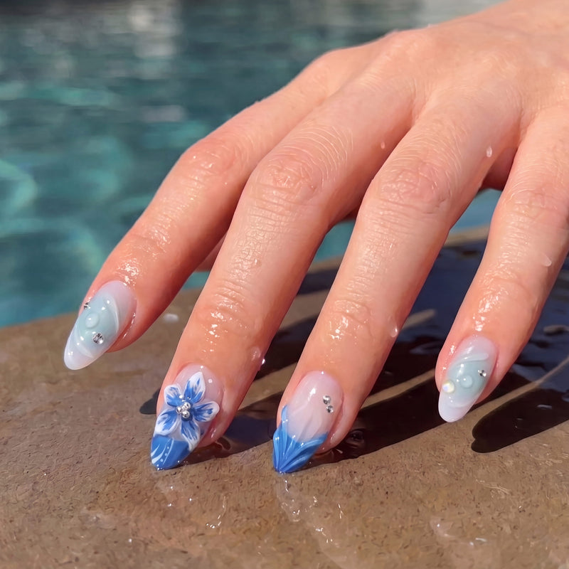 Poolside hand model wearing Azure Bloom press-on nails with a sculpted blue flower, blue tips, and aqua swirl details