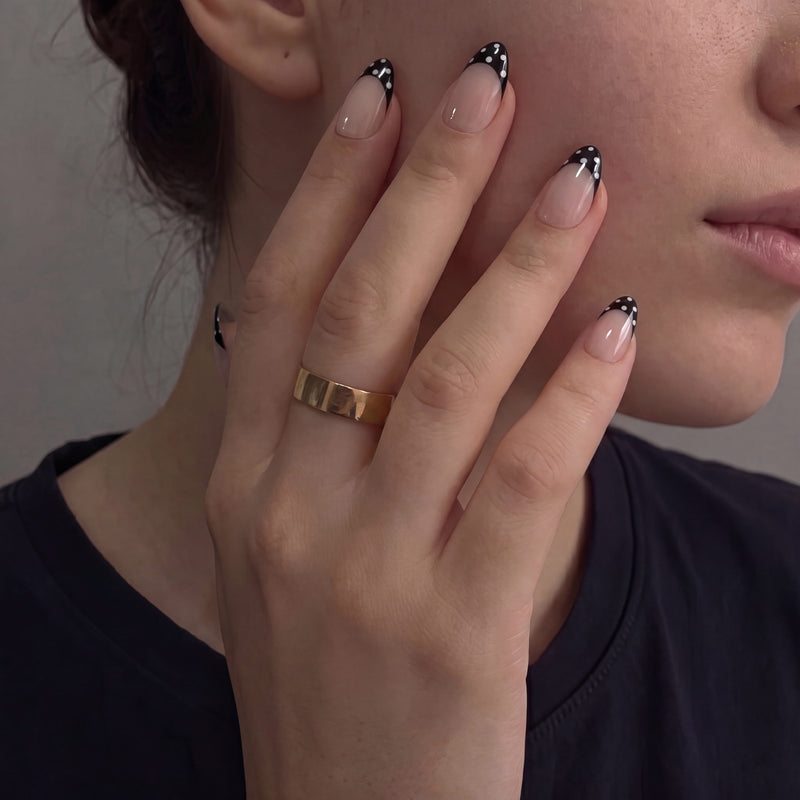 Close-up of a hand model wearing Bare Polka press-on nails in nude pink with black polka dot tips