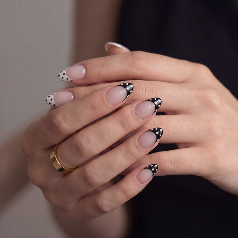 Hand model wearing Bare Polka press-on nails in nude pink with black polka dot tips, shown with hands stacked together