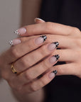 Hand model wearing Bare Polka press-on nails in nude pink with black polka dot tips, shown with hands stacked together