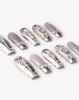 Angled flat lay of Baroque Crown press-on nails with silver chrome accents, white scrollwork, pearl details, and rhinestone crown charms