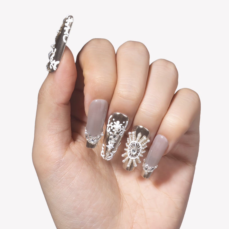 Close-up hand model wearing Baroque Crown press-on nails with silver chrome tips, white baroque scrollwork, pearls, and rhinestone crown details