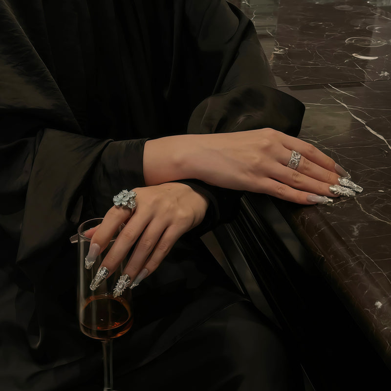 Tabletop lifestyle image of a hand model wearing Baroque Crown press-on nails with silver chrome, pearls, rhinestones, and white baroque accents