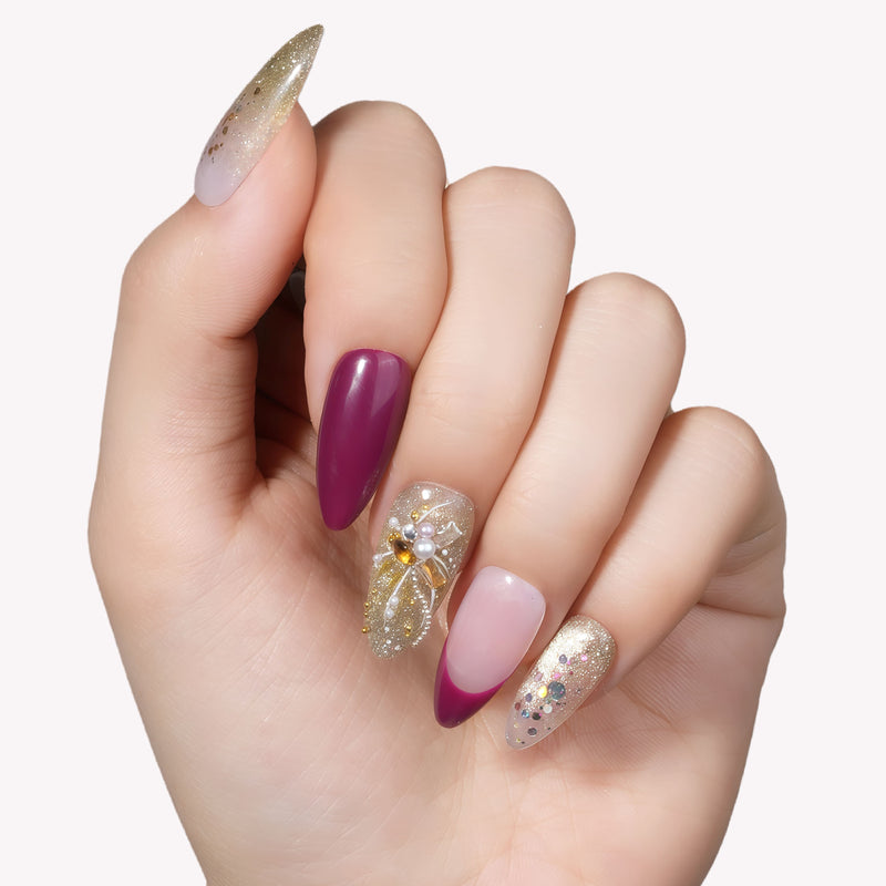Hand model wearing Berry Firelight press-on nails with burgundy tips, gold glitter accents, and gemstone details