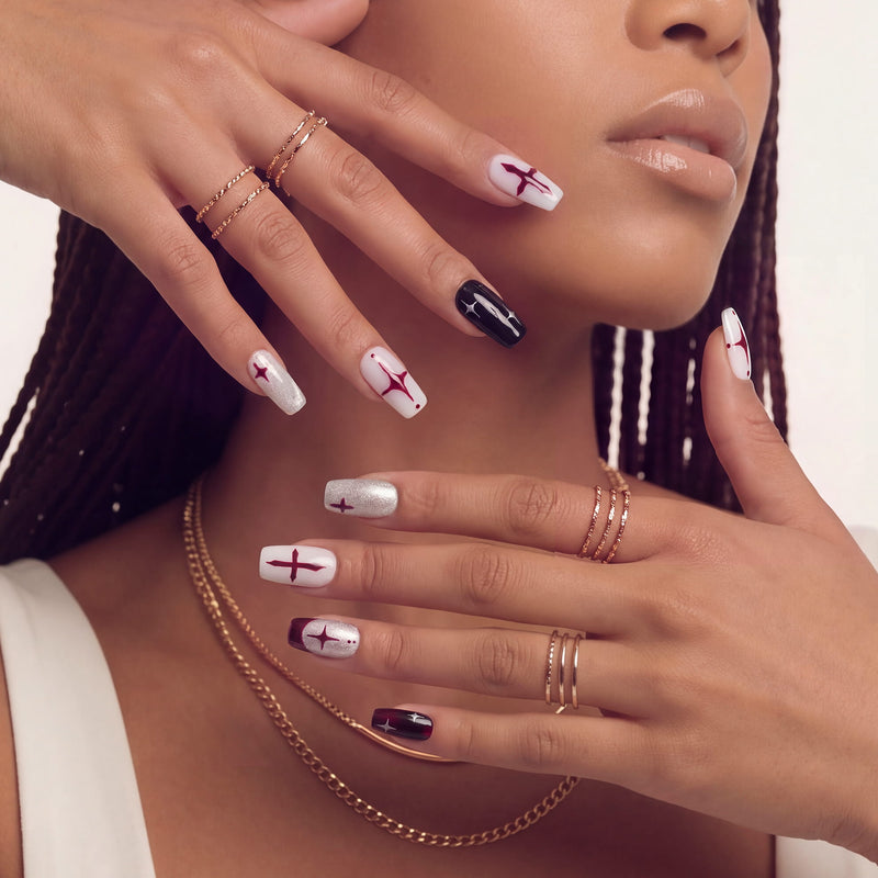 Face close-up hand model wearing Blood Moon Cross press-on nails with black, white, silver glitter, and burgundy designs, cross starburst accents, and glossy square shapes