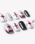 Flat lay of Blood Moon Cross press-on nails with black, white, silver glitter, and burgundy designs, cross starburst accents, curved moon tips, and glossy square shapes