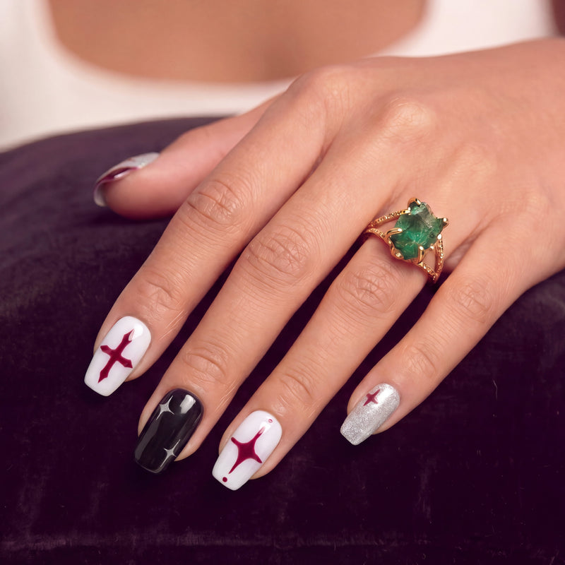 Hand model wearing Blood Moon Cross press-on nails with white, black, silver glitter, and burgundy designs, cross starburst accents, and glossy square shapes